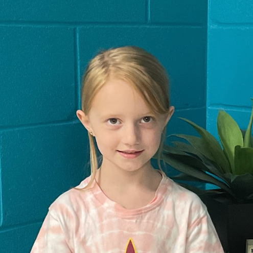 Cameron Seward wearing a pink tie dye shirt in front of a turquoise wall and a plant behind her