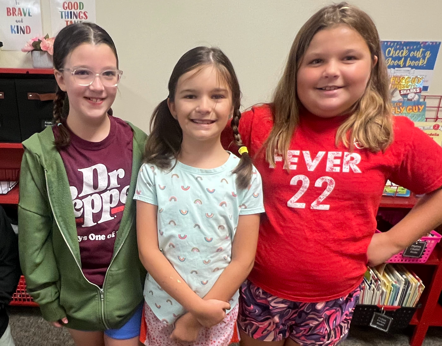 Four students standing together in the classrooms; text on tshirts say NBA, Dr. Pepper, Fever22