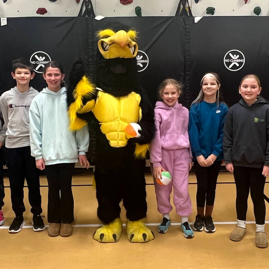 Students standing with the MP Mascot Herschel in the school gym; one sweatshirt text says Champion