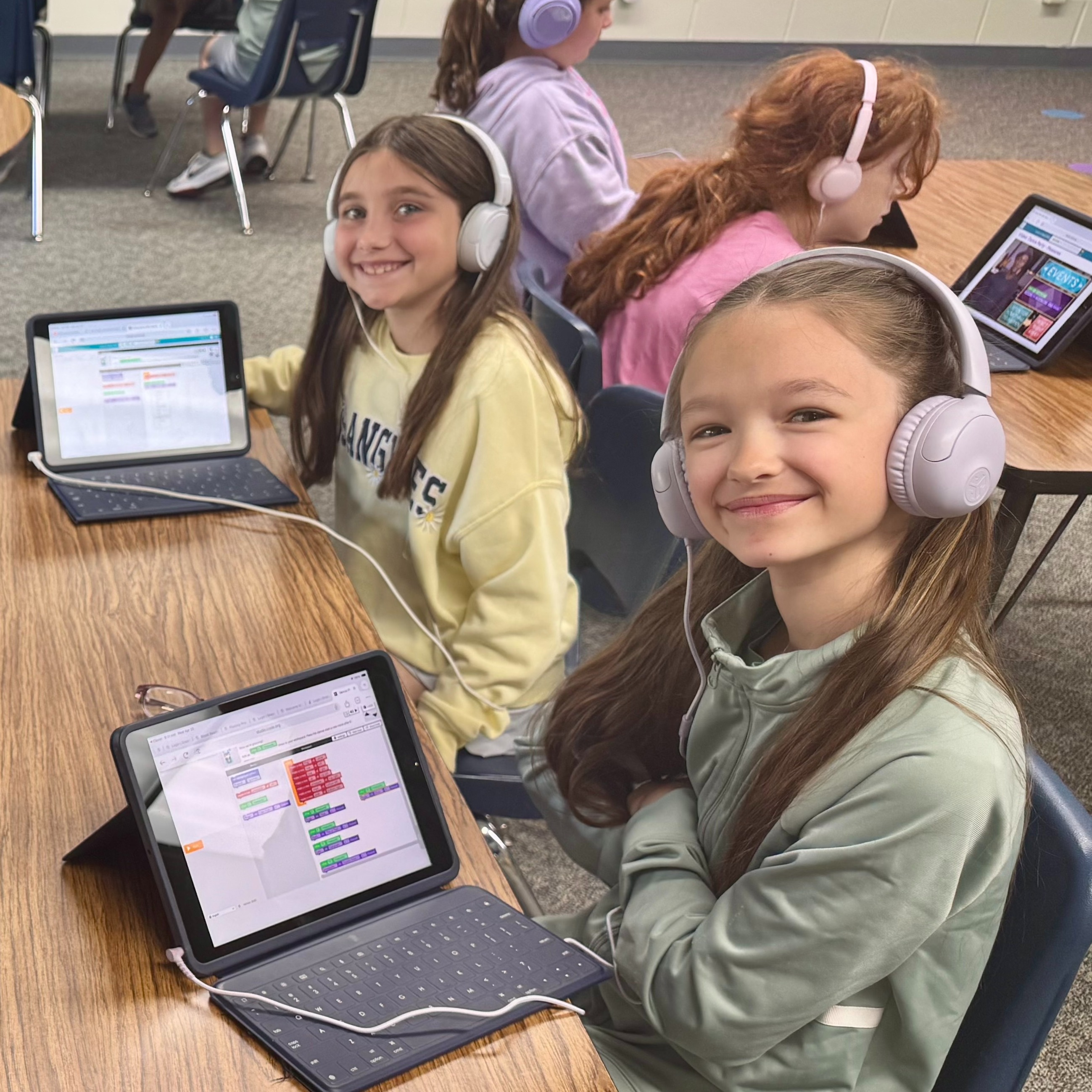 Students sitting at tables with ipads working on a coding application wearing headphones plugged into each ipad
