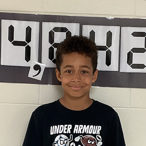 Jay - West Elementary Student standing in front of a bulletin board that reads 14,842
