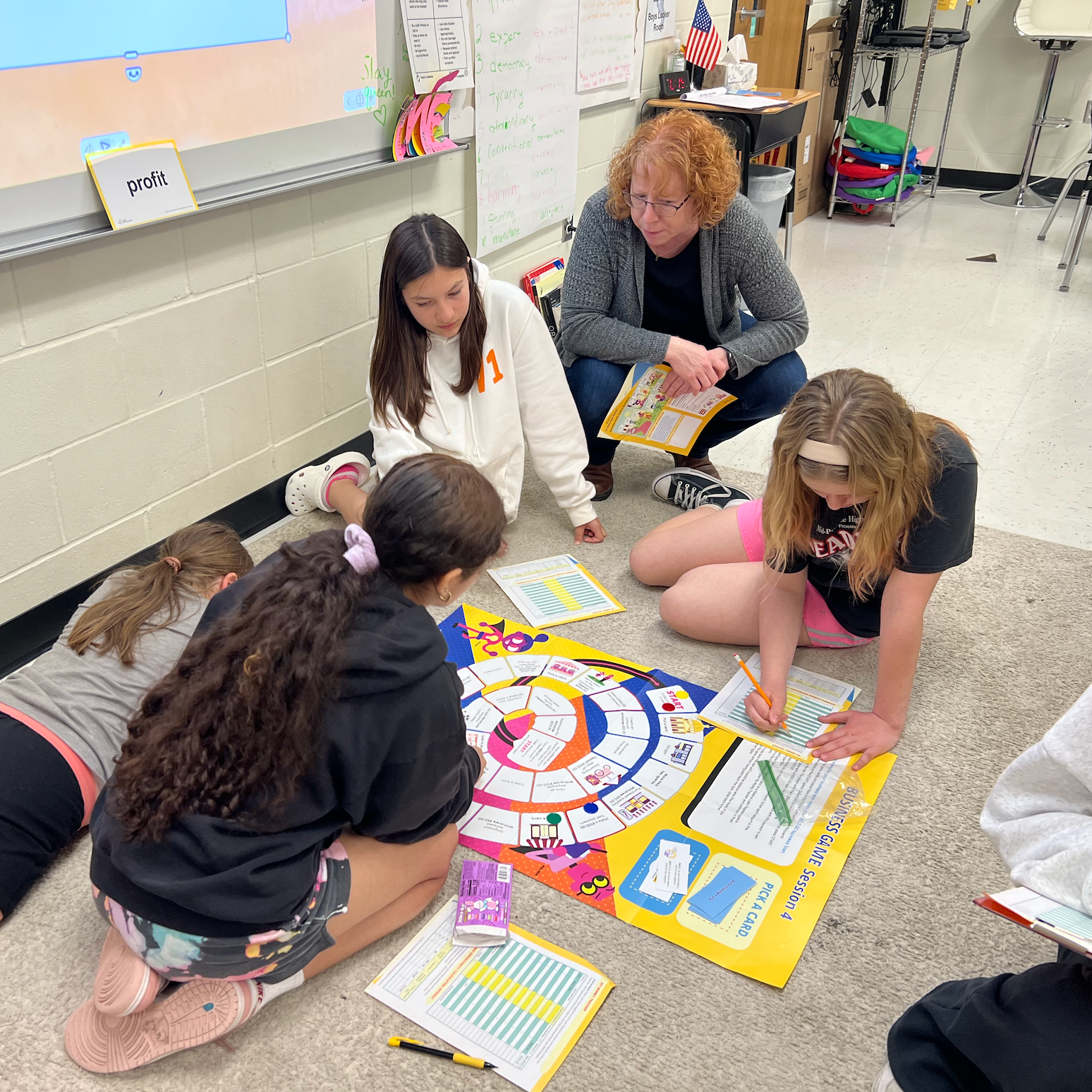 Students playing a financial literacy board game on the classroom floor with a community volunteer