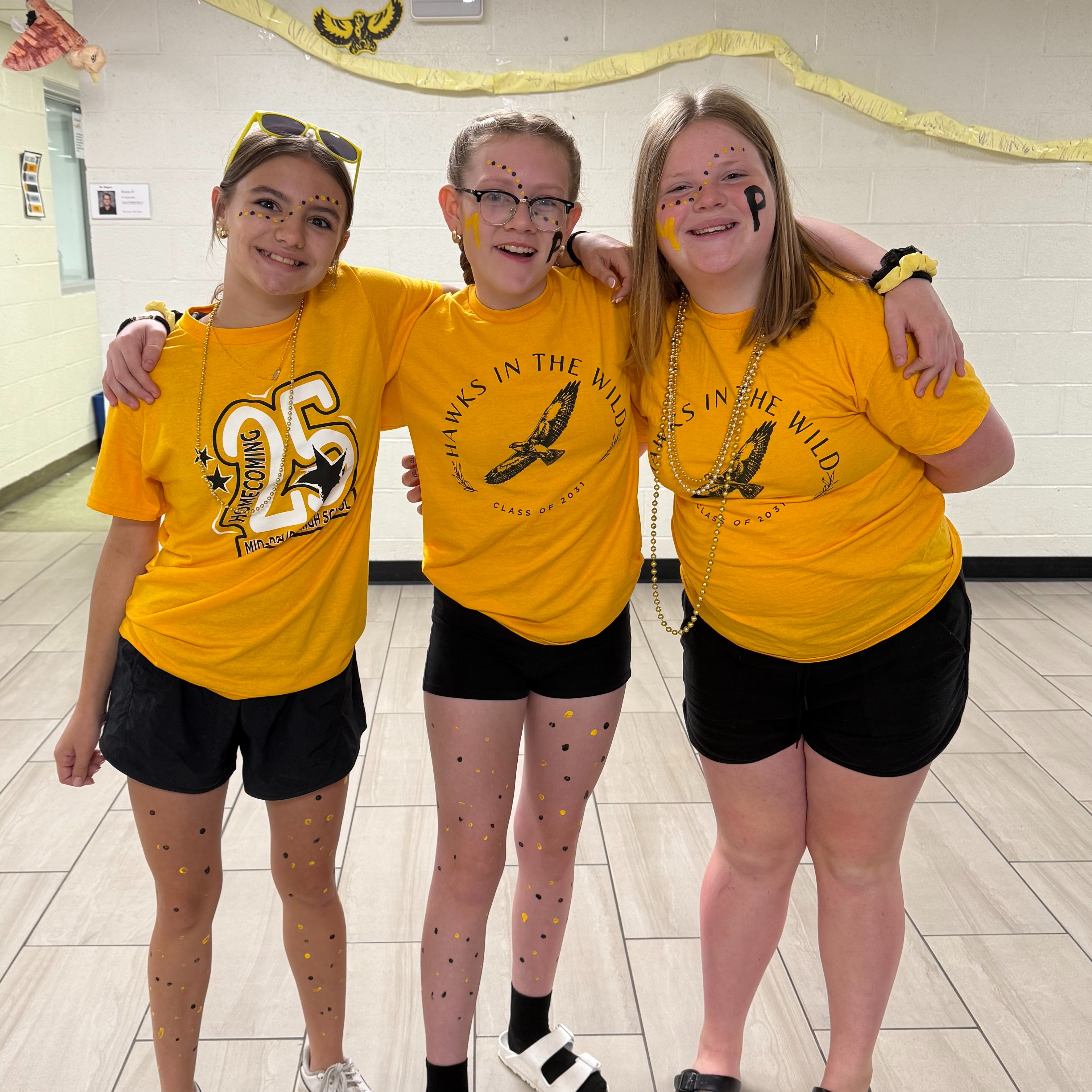 Three female students with arms around each other smiling, Text on shirts read 25 and Golden Hawks in the Wild