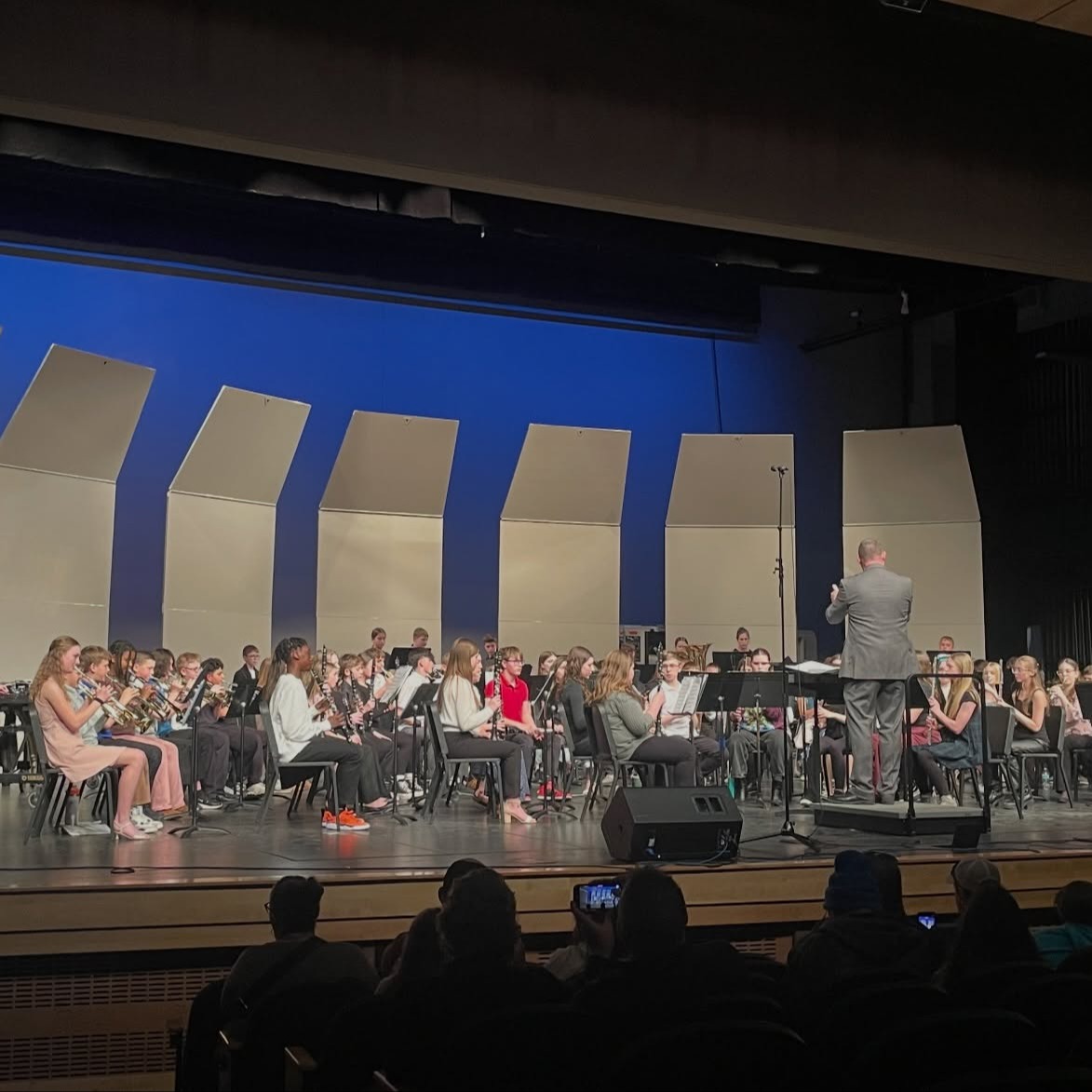 Large group middle school band members seated together playing instruments with band director up front directing the song