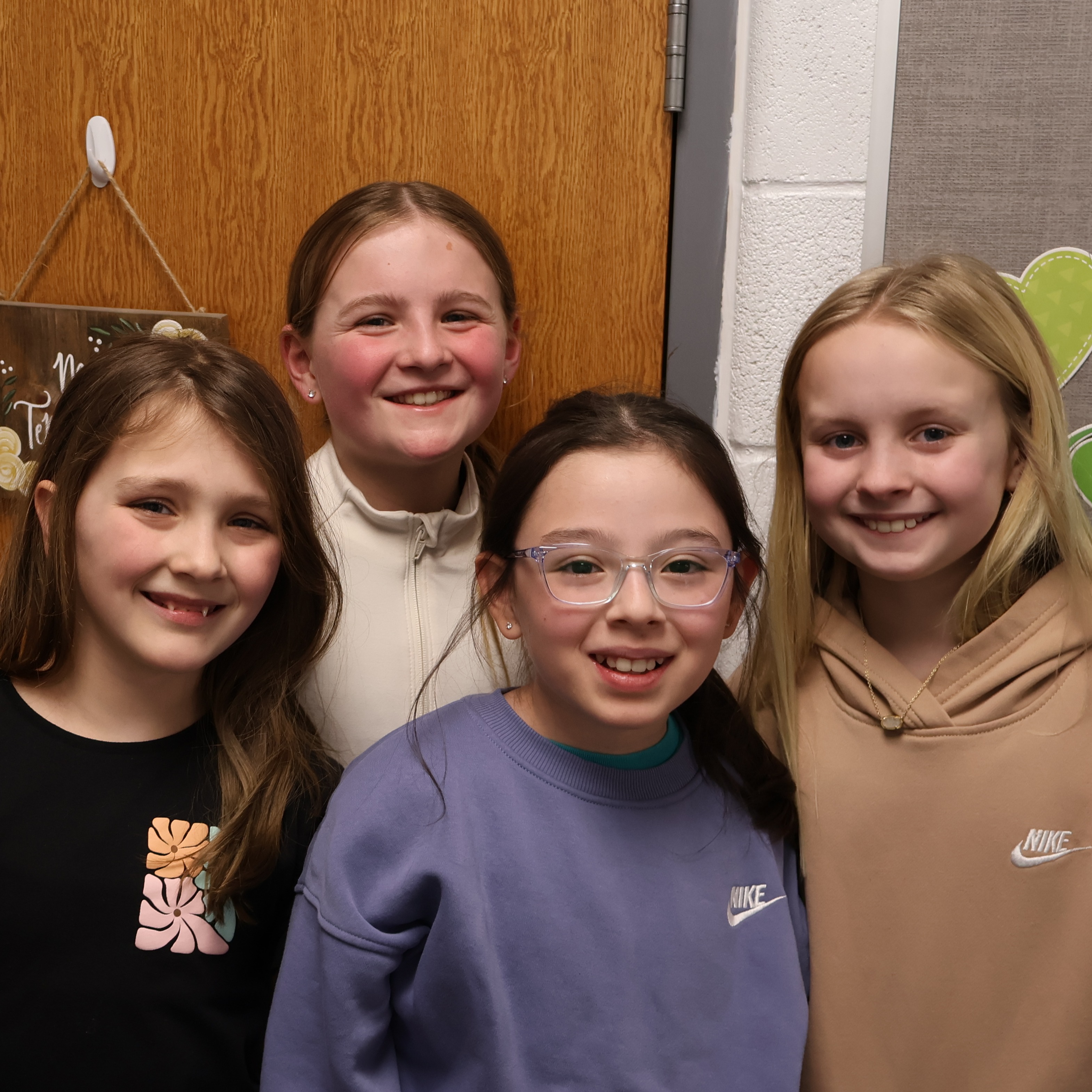 Four female students standing as a group smiling in front of their classroom door