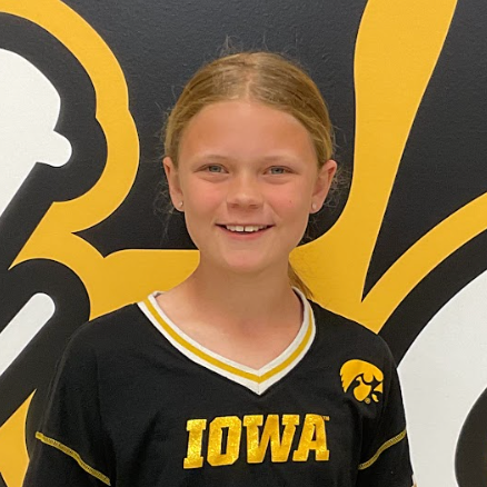 Rose Hammes, MP Middle School student wearing a black and gold shirt with the Iowa Hawk on it in front of the MP hawk wall decal