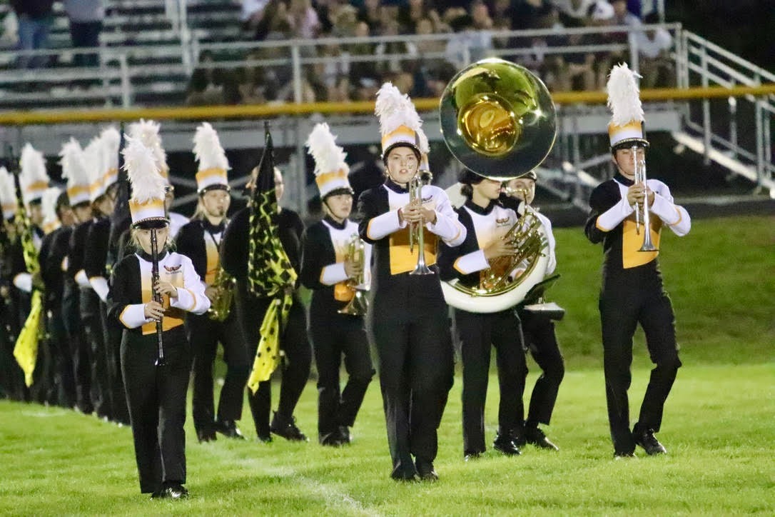 high school marching band marching out onto the field holding each of their instruments out front in black and gold Golden Hawk uniforms