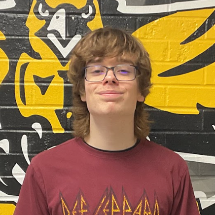 Parker Thomas wearing a burgundy shirt with Def Leppard text in gold standing in front of the MP hawk wall decal