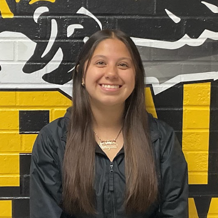Maya wearing a black jacket standing in front of the MP hawk wall decal