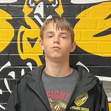 Mac wearing a grey t-shirt with red writing that says Fight and a black jacket standing in front of the MP hawk wall decal