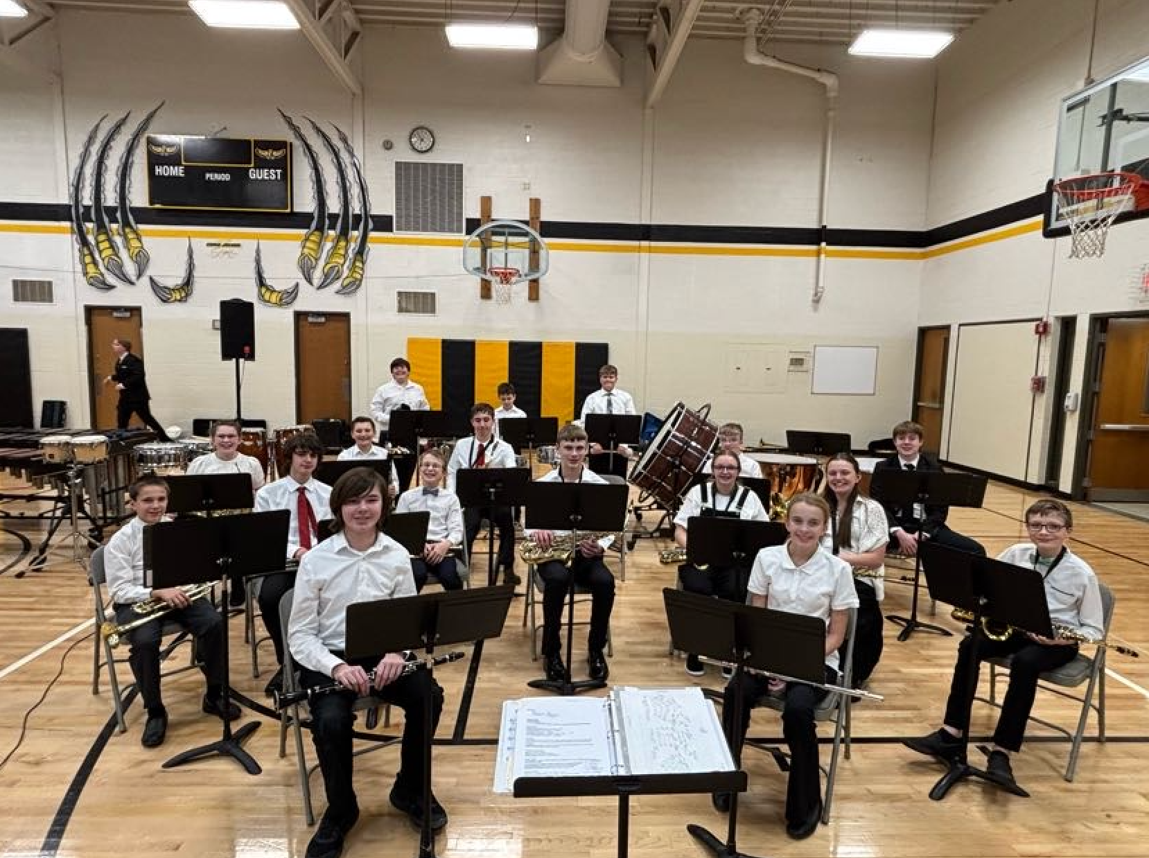 Band students sitting in chairs with music stands in front o fthem in the school gym holding their instruments
