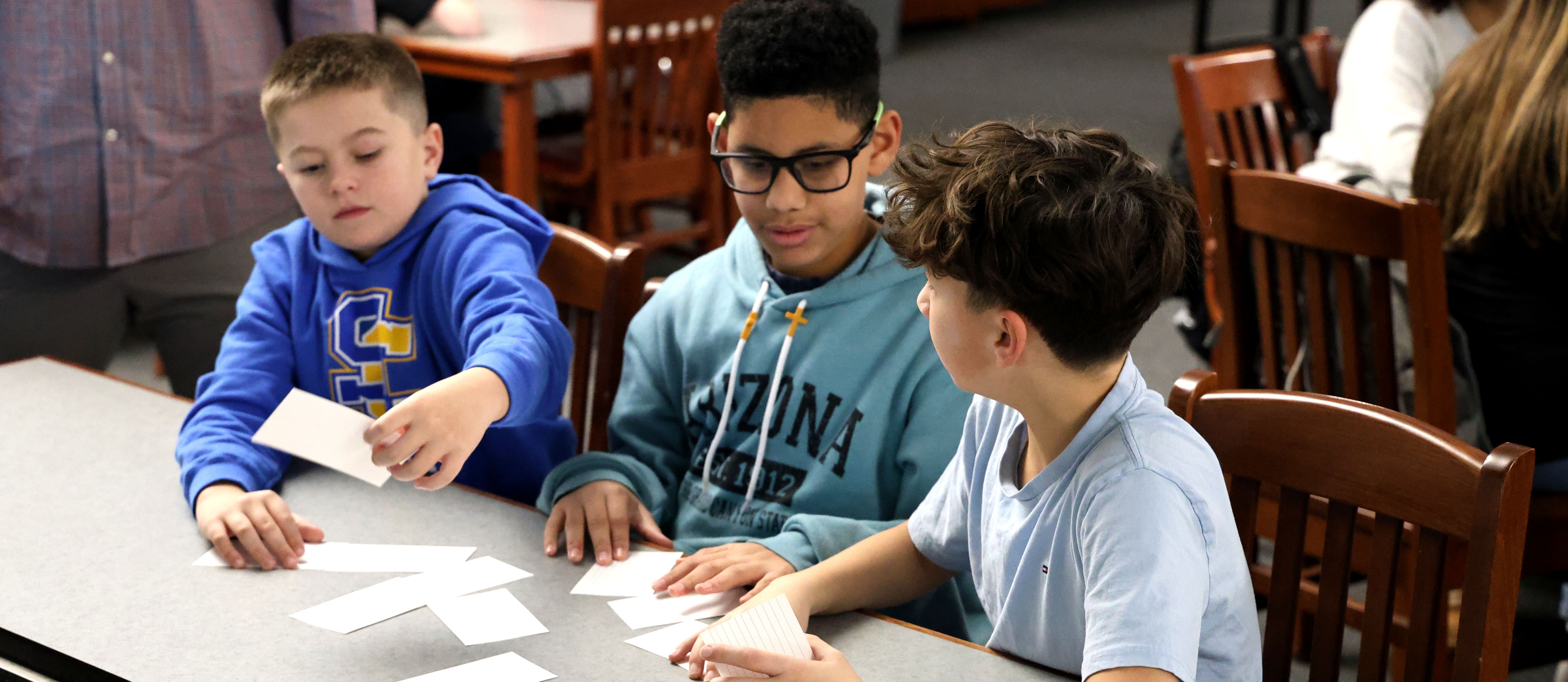 Three boys sitting at a table with index cards
