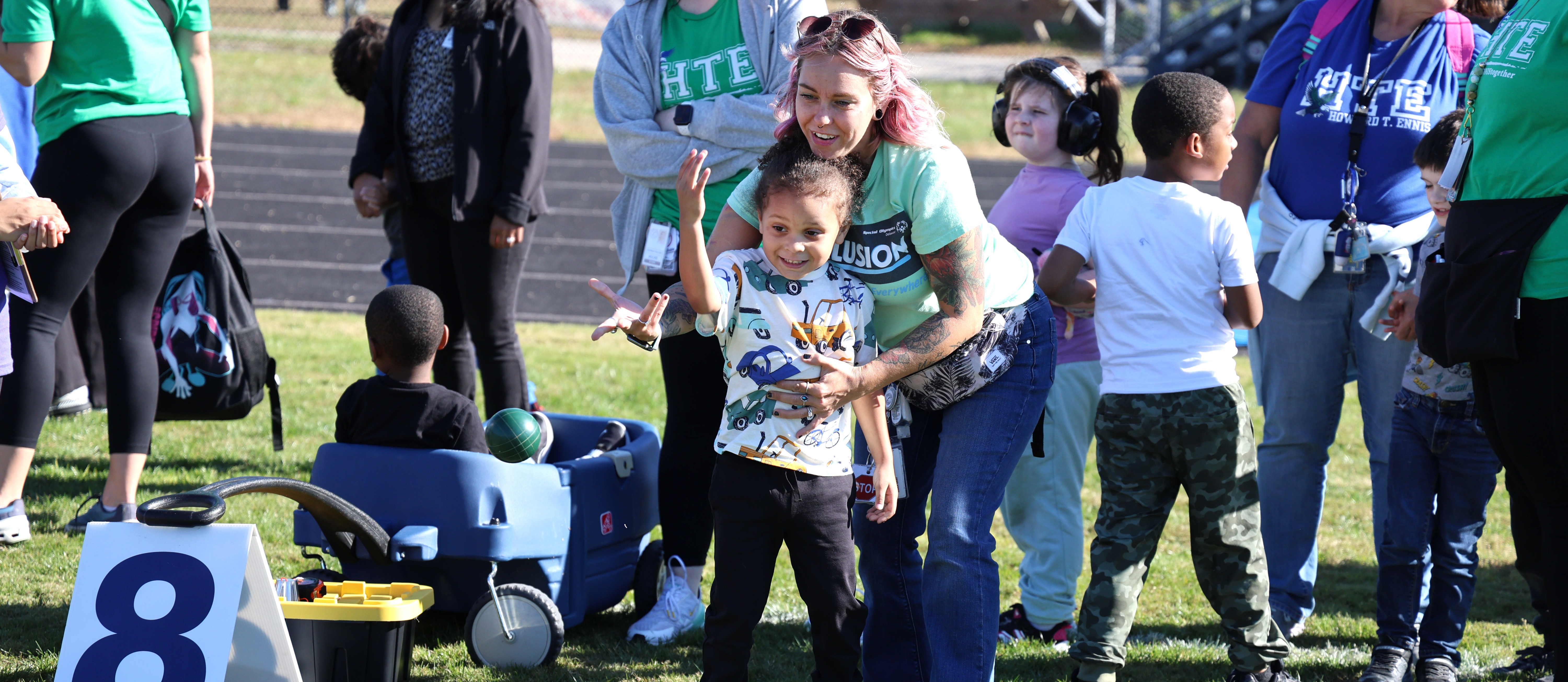 Staff member helping a student throw a ball in a grassy area