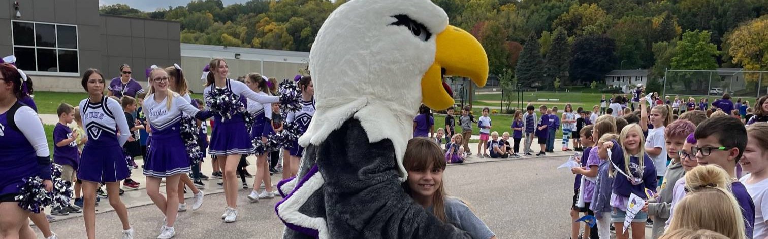 Little girl hugging eagle mascot at pep fest.