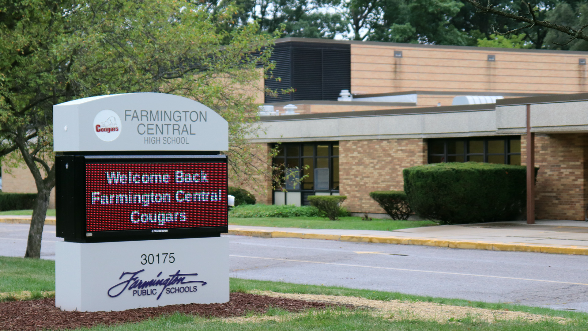Electronic sign outside Farmington Central High School welcoming back Cougars with school building in background.