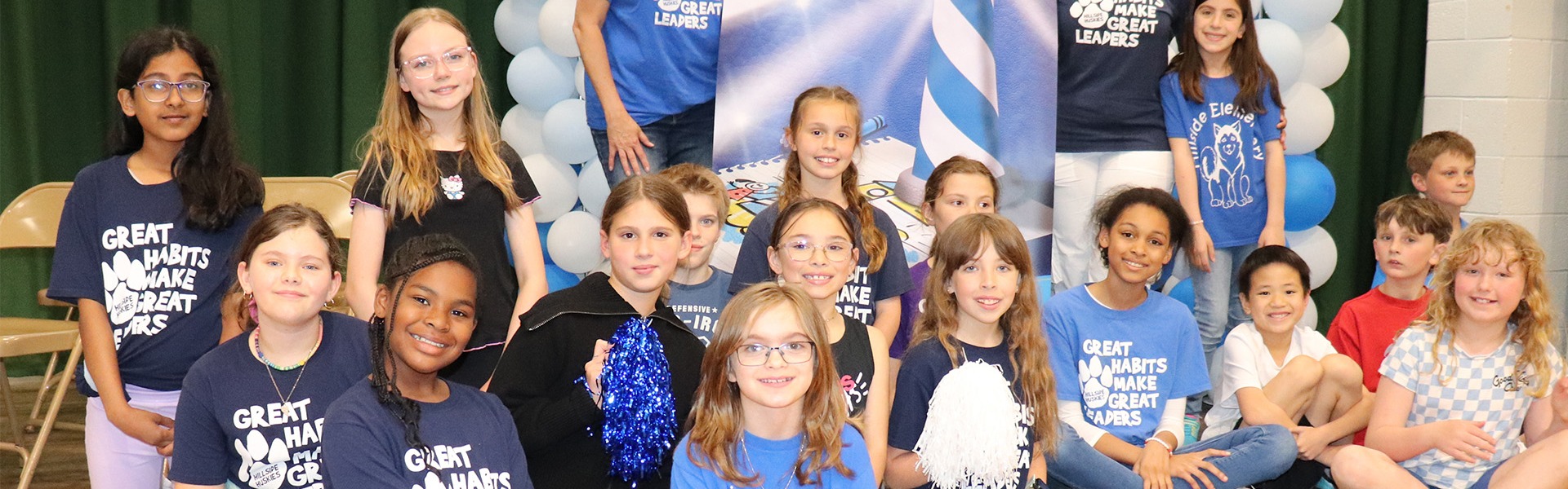 Group of elementary students posing in front of a Leader In Me Lighthouse School banner with blue and white balloons.