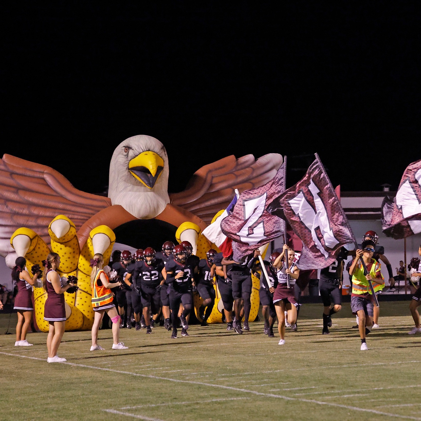 Cheerleaders and football players running out of a blown up Eagle