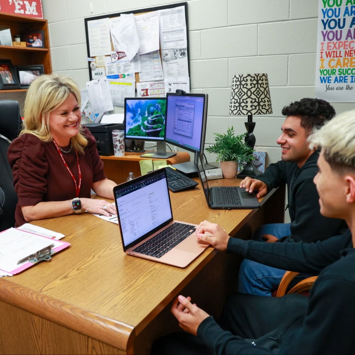 Counselor sits with two students on laptops