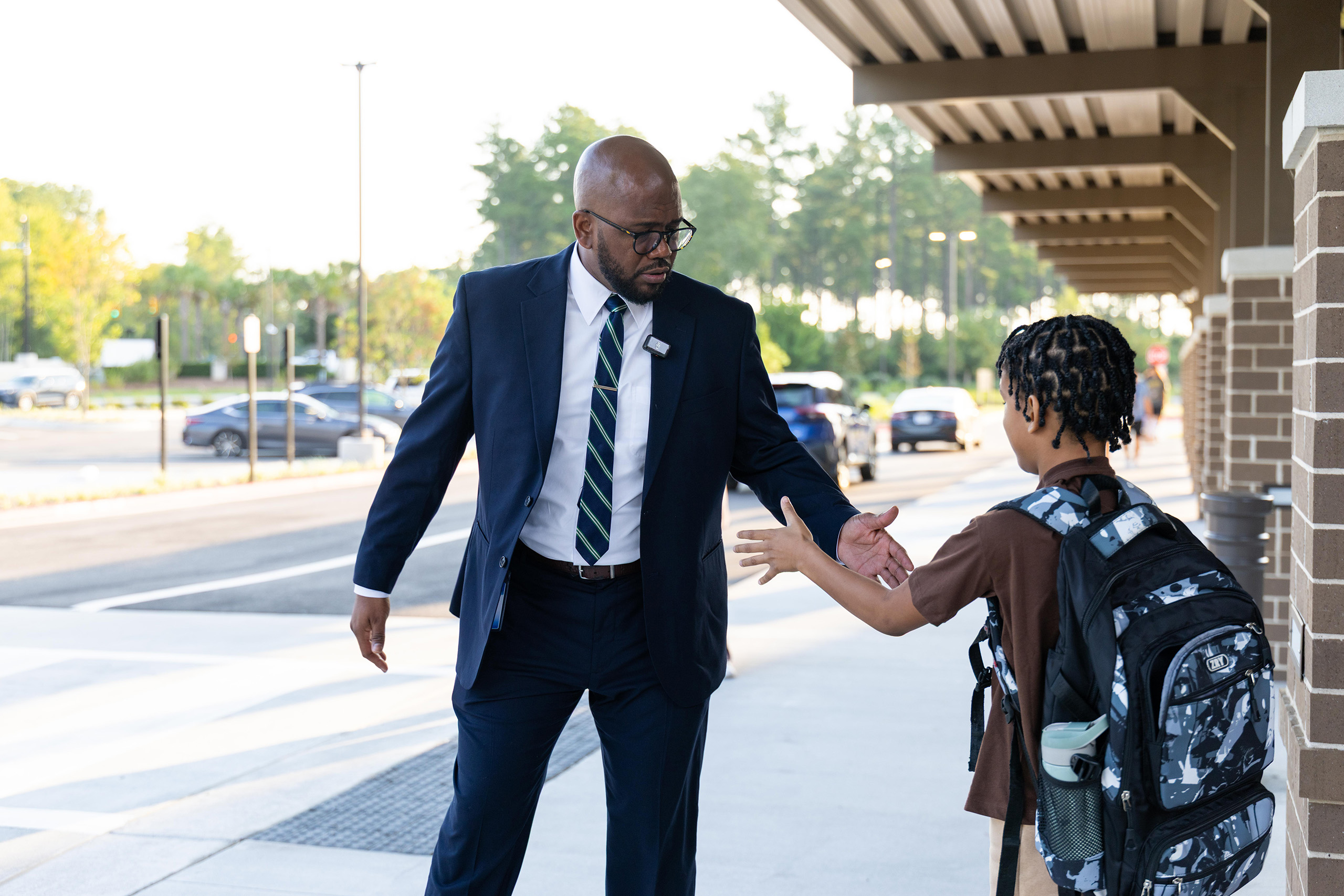 A man and a child are standing outside. The man shakes the child's hand. They are in front of a building.