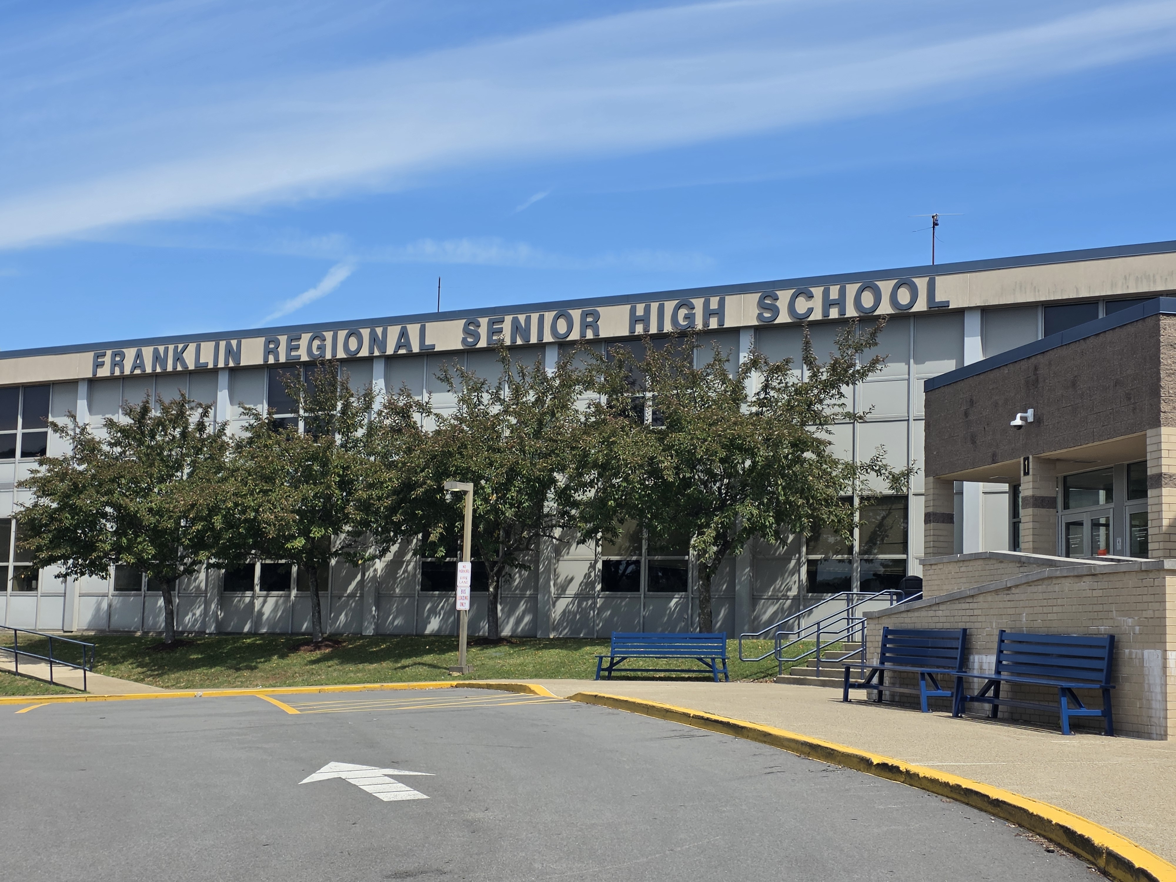 Building with text "Franklin Regional Senior High School" in front of trees and blue benches.