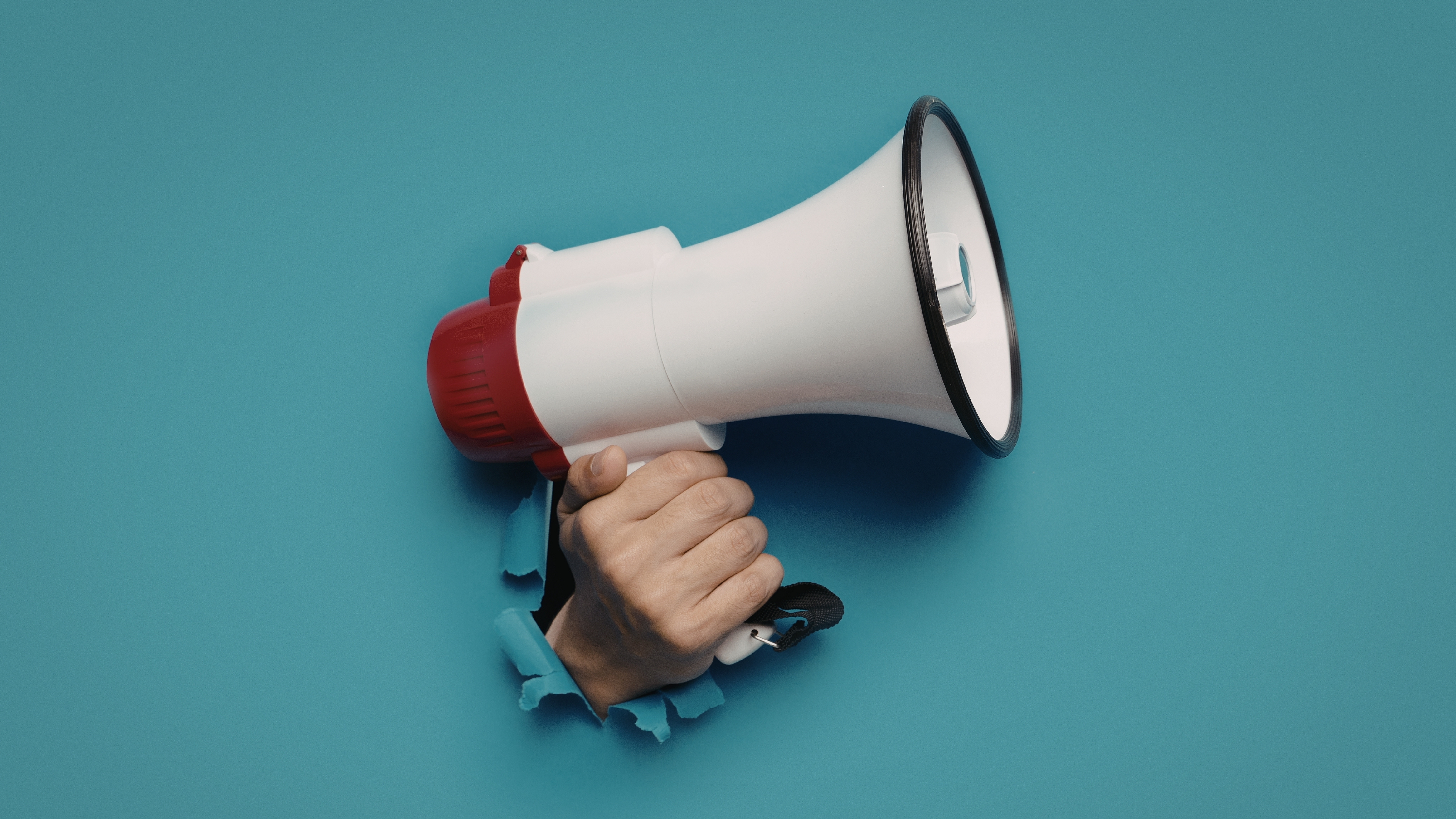 Hand holding a megaphone through a torn paper on a blue background.