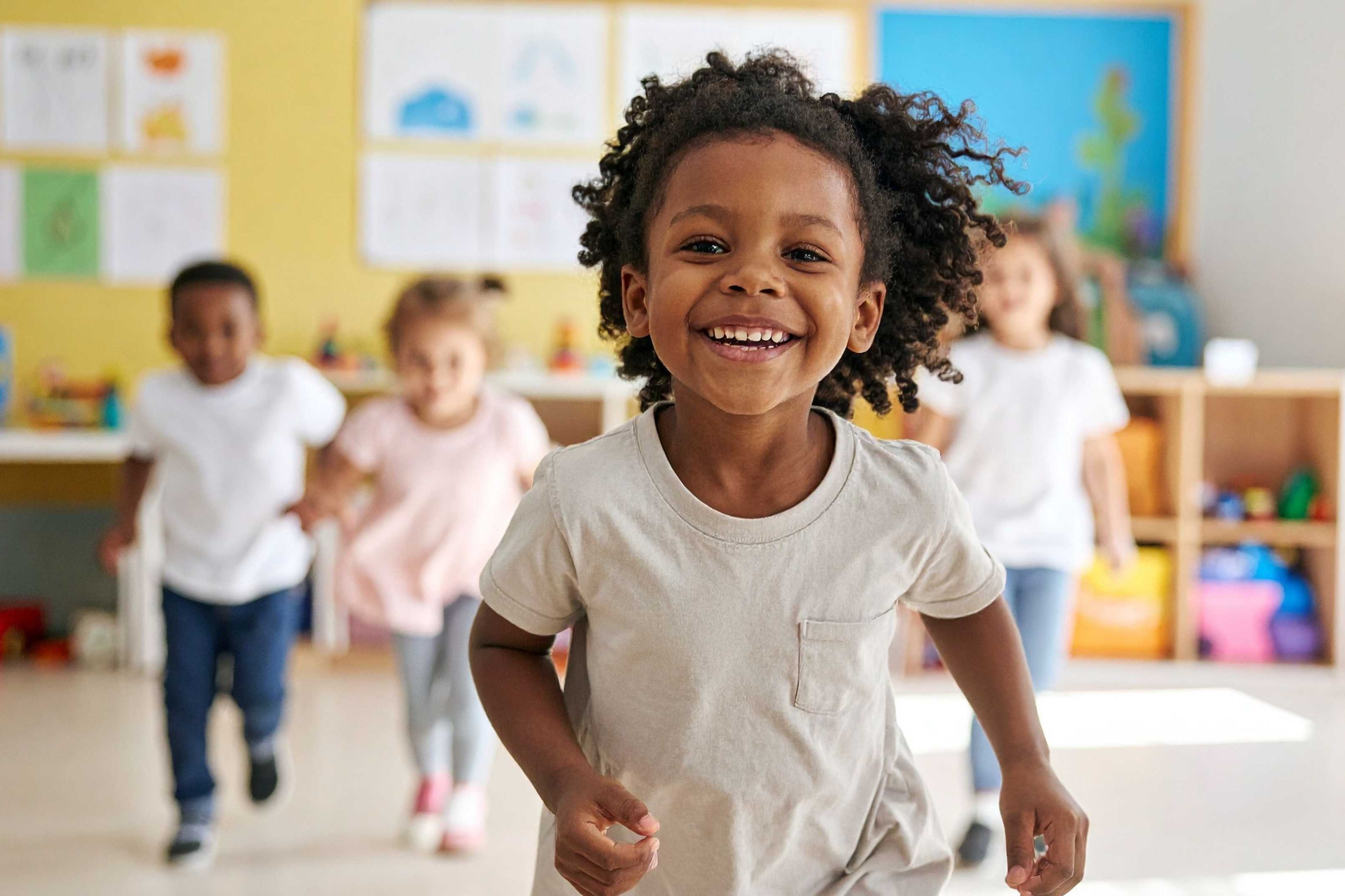 Kids run in a playroom with yellow walls and various toys and learning materials.