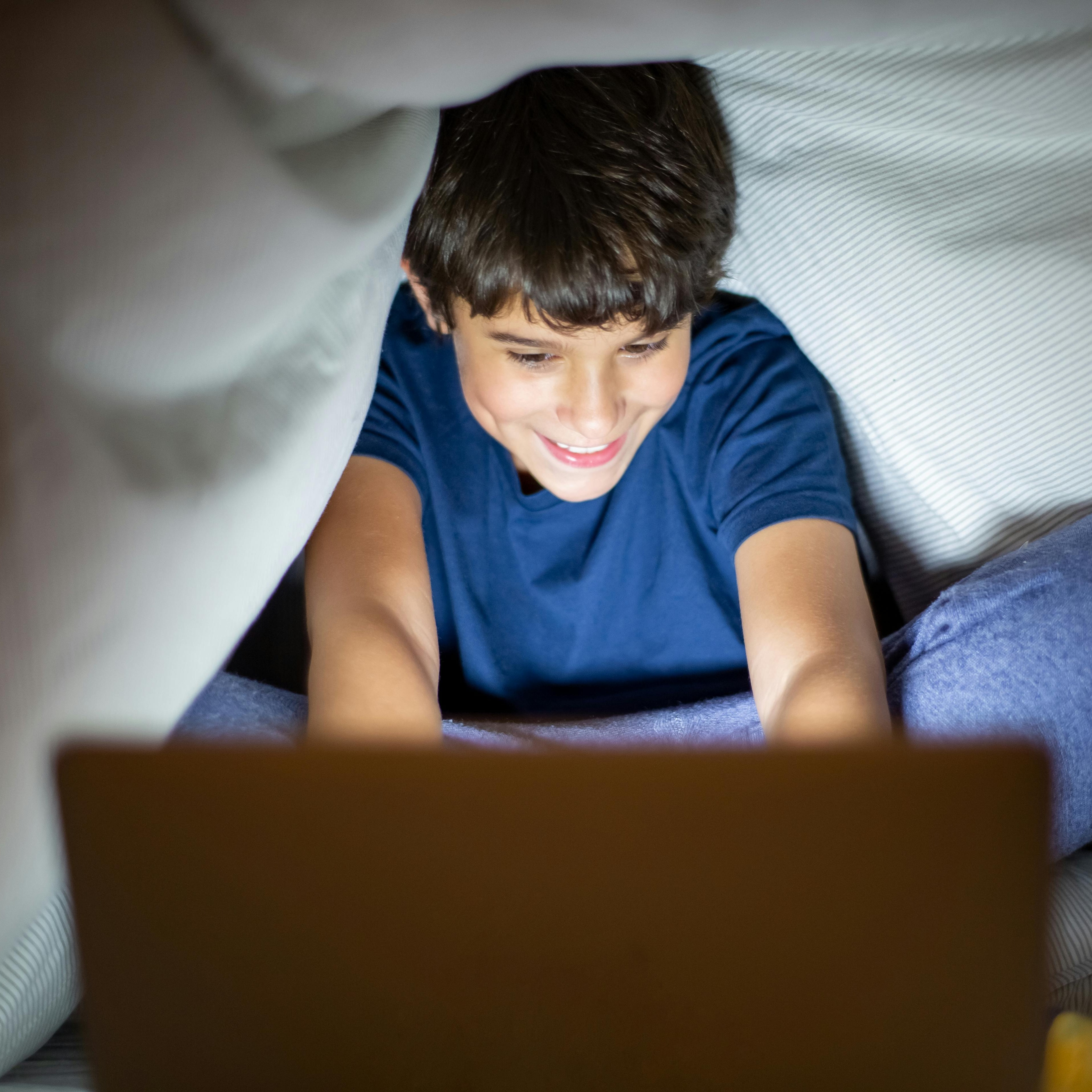 Boy working on computer under bed covers