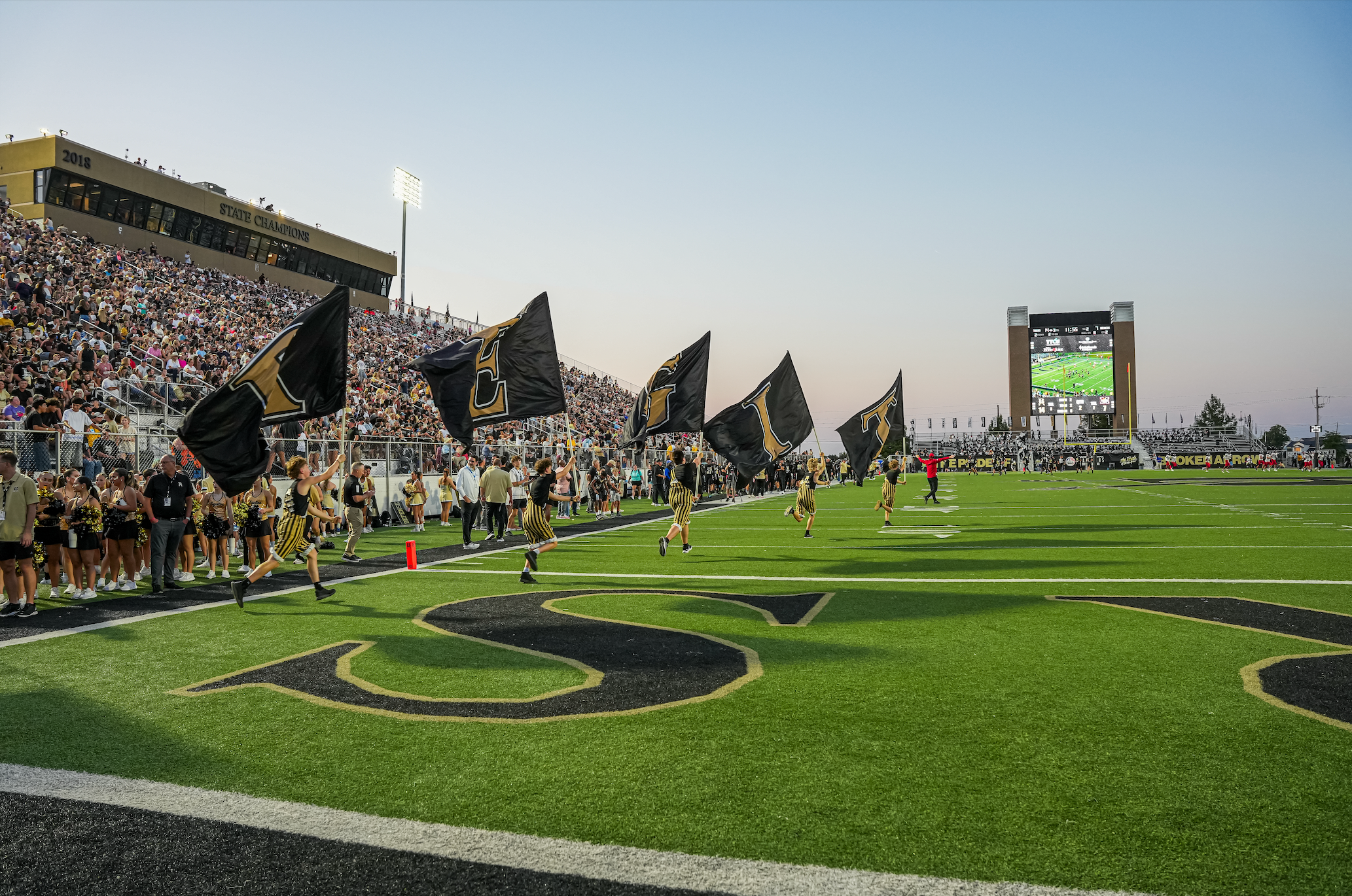 Students running on football field with T.I.G.E.R.S. flags