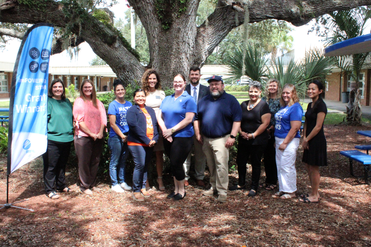 group of people smiling for a picture outside under a tree
