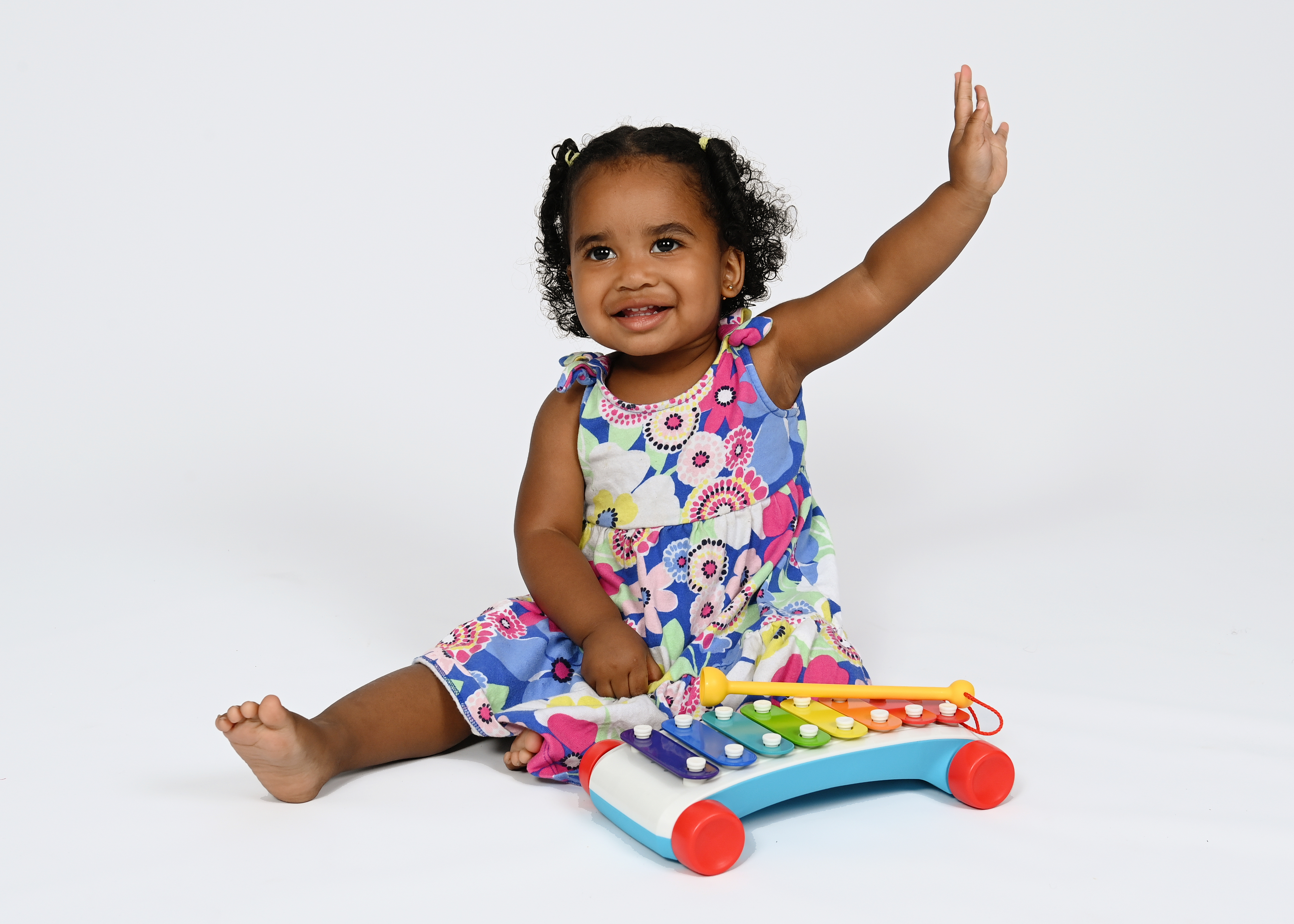 A young child in a colorful floral dress sits and plays with a colorful xylophone.