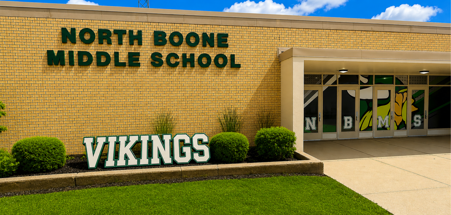 Exterior of North Boone Middle School, featuring yellow brick walls, a green "VIKINGS" yard sign, and "NBMS" lettered on the glass doors.