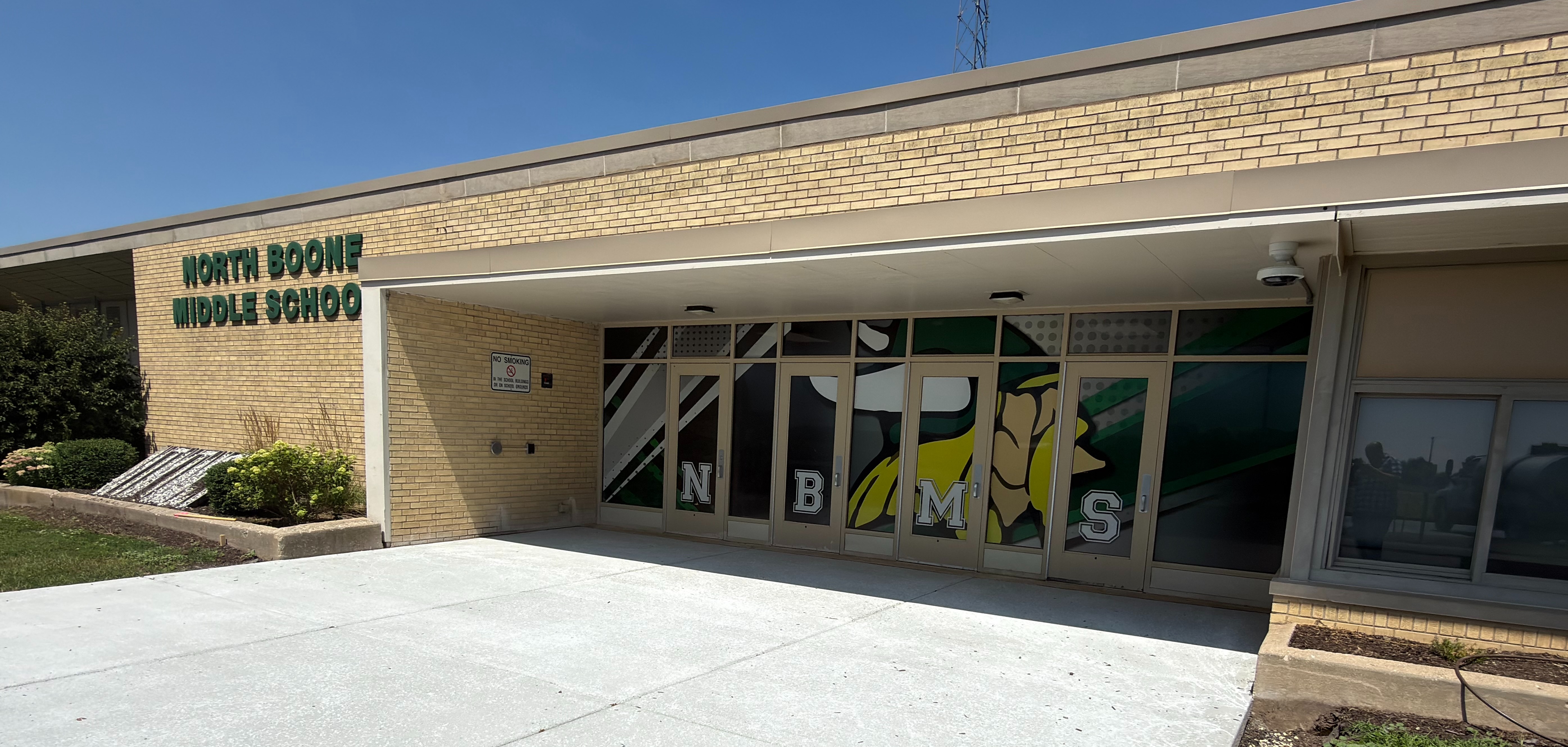 Exterior of North Boone Middle School, featuring yellow brick walls, a green "VIKINGS" yard sign, and "NBMS" lettered on the glass doors.