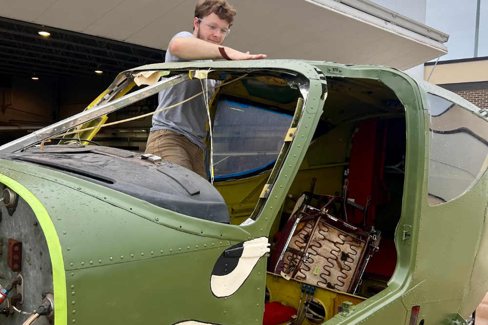 Aviation Maintenance student working on a the cockpit of a green airplane. 