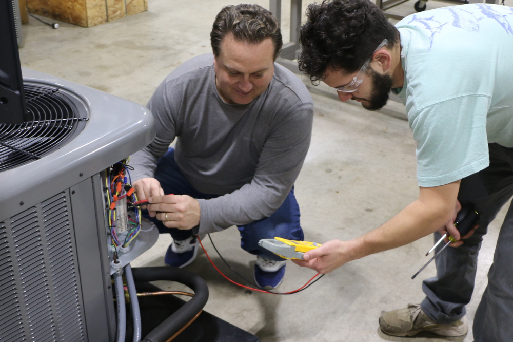 HVAC instructor and student work in air conditioning unit. 