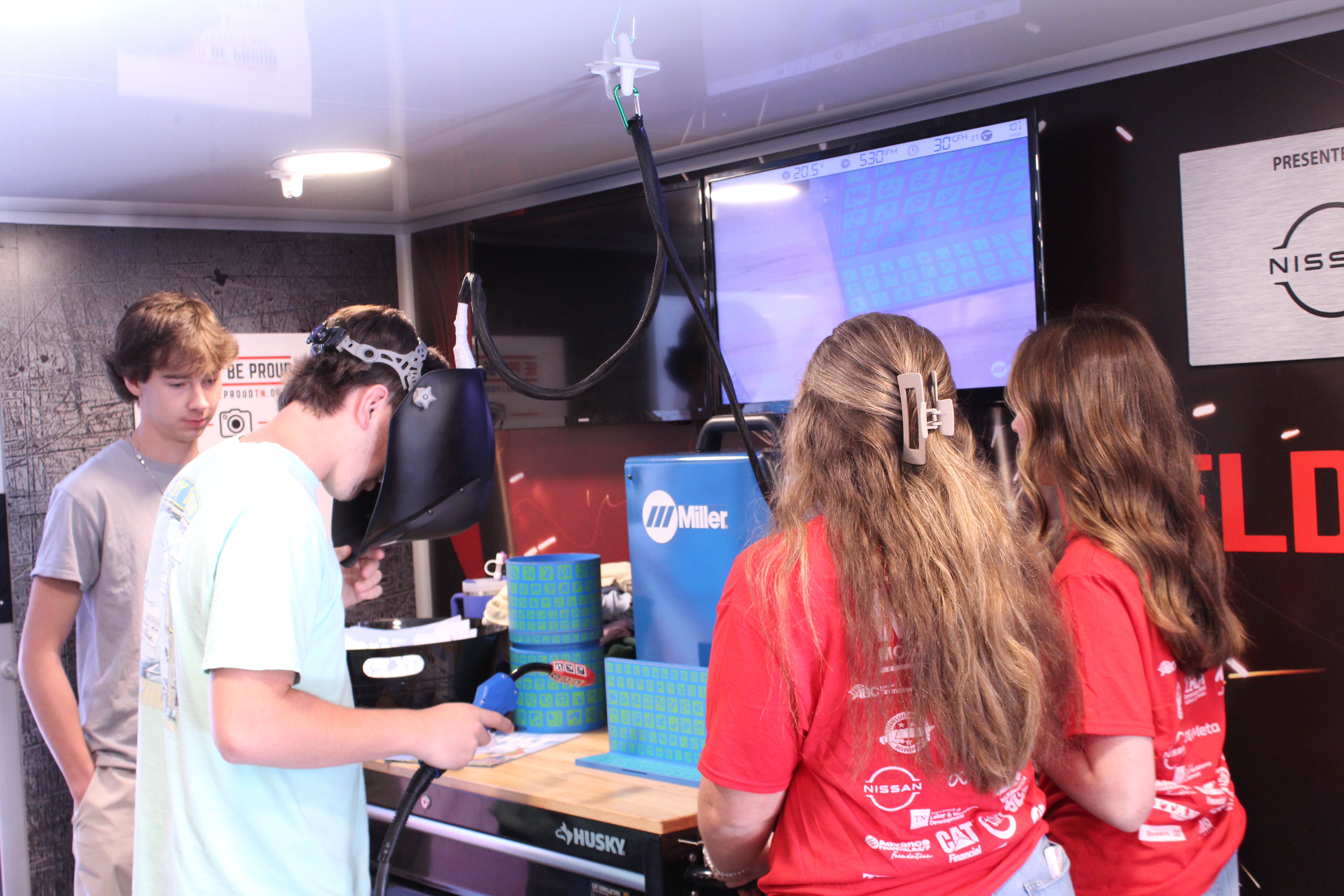 A student tries his hand at a welding simulator while 3 other students watch.