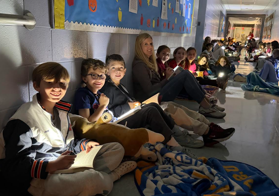 students and teachers reading books in a dark hallway with flashlights