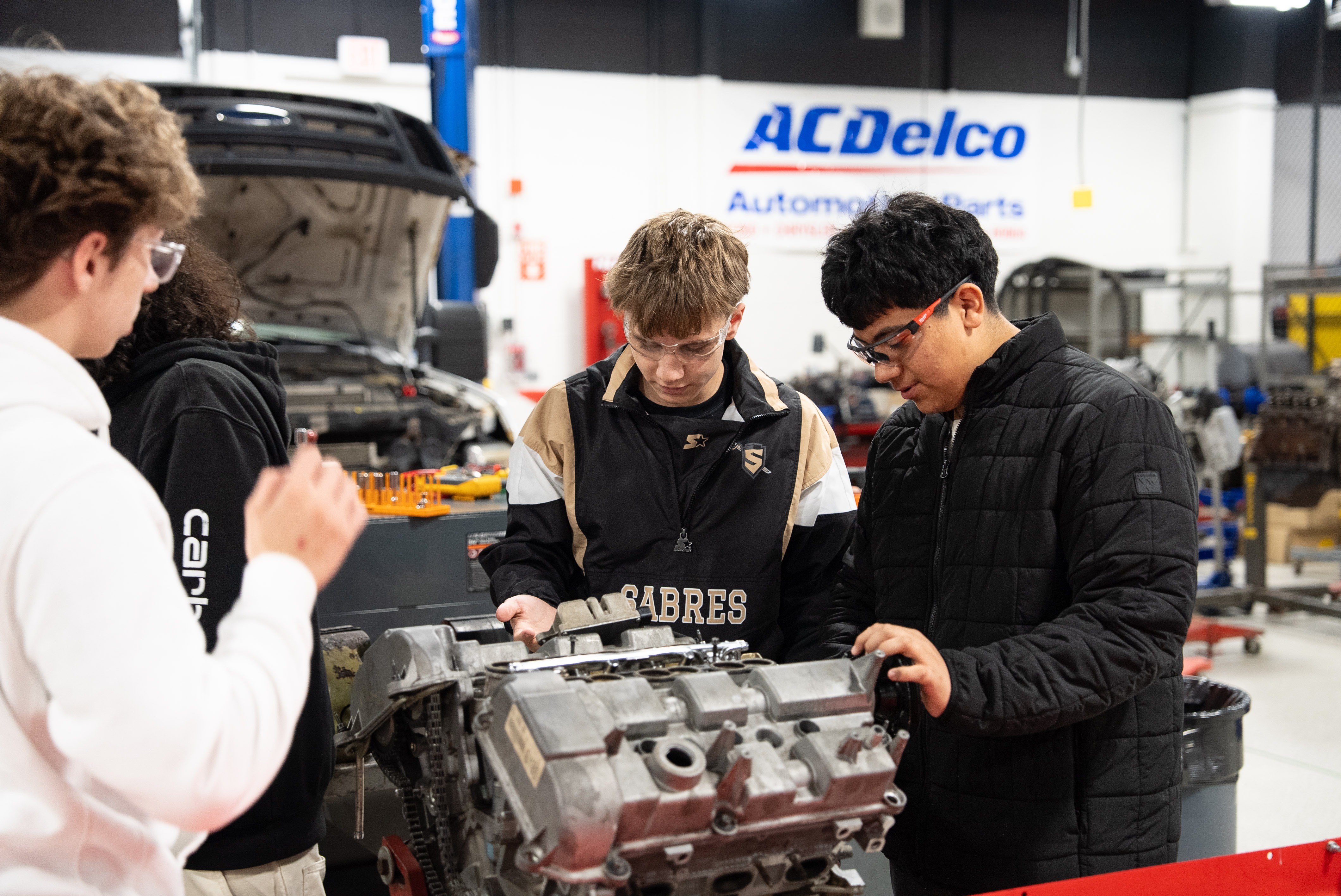 Three high school students work on an engine in an automotive lab. 
