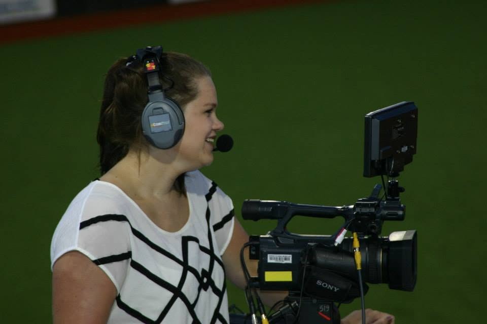  A student wears audio headphones while looking through a camera at a sporting event.