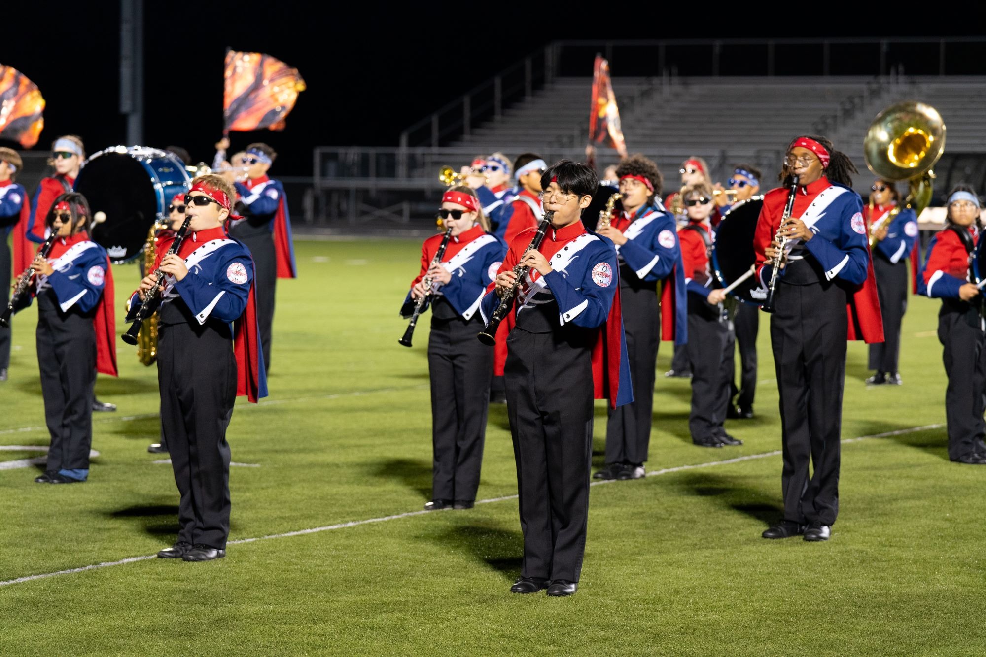 A high school marching band wears red, white and blue as they play on the field. 