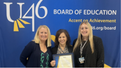 Three women from the U-46 Financial Services Department stand in front of a blue U-46 Board of Education Accent on Achievement backdrop. The middle woman holds a framed award.