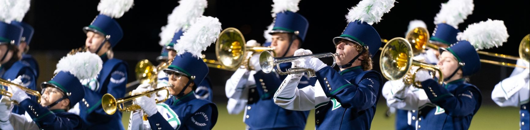 A marching band performs on a field. They wear matching blue uniforms and play brass instruments.