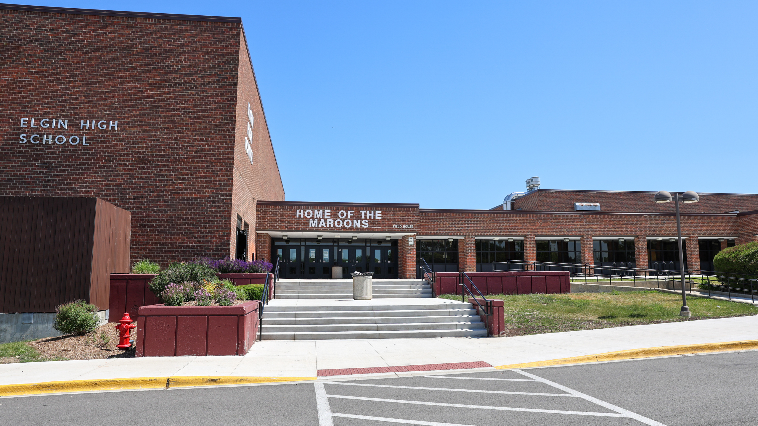 A brick school building with "Elgin High School" and "Home of the Maroons" in bold letters. A red fire hydrant.