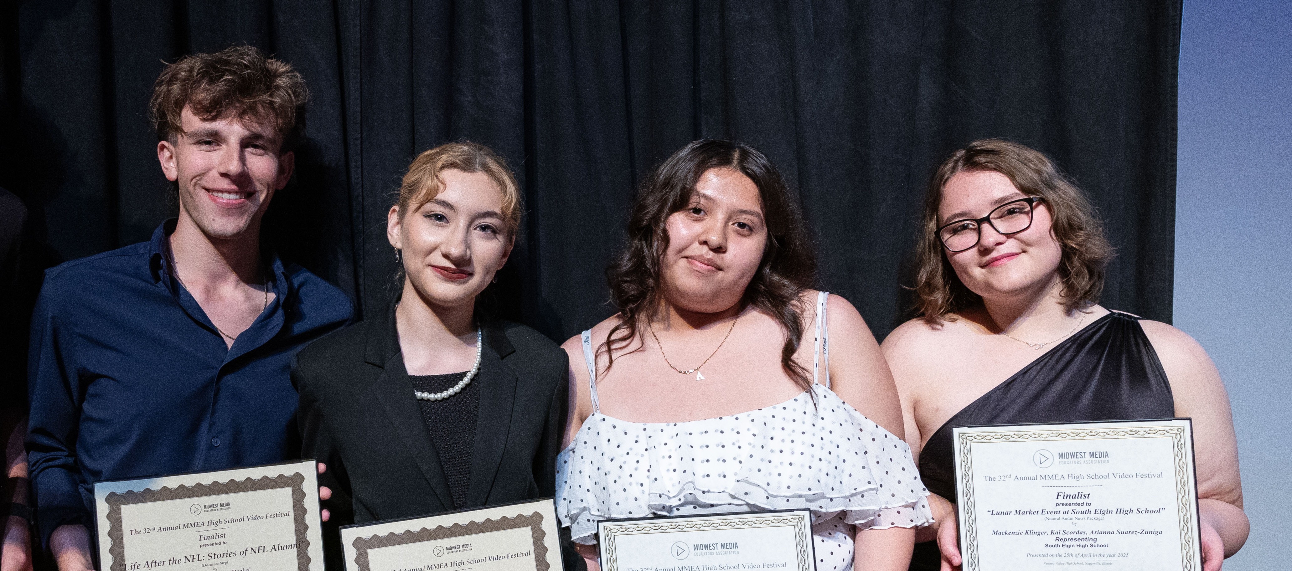 Five young adults stand on a stage, holding certificates, and smiling. The background is black.