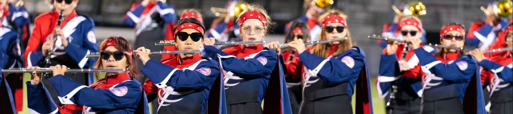 A group of people dressed in matching uniforms performs on a field with various instruments.