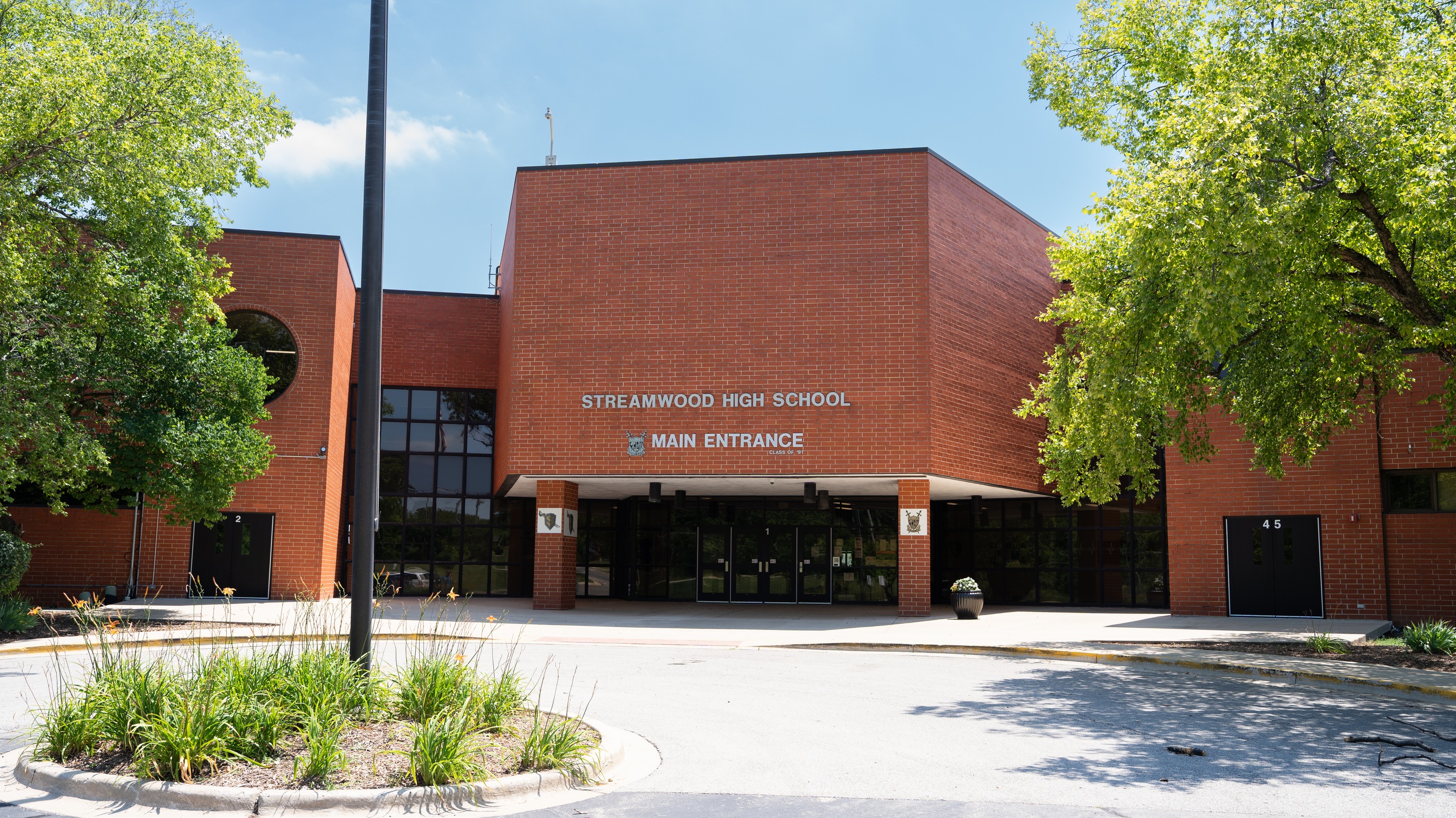 A modern, red brick building with arched windows. It reads "High School" above the main entrance. Trees surround the area.