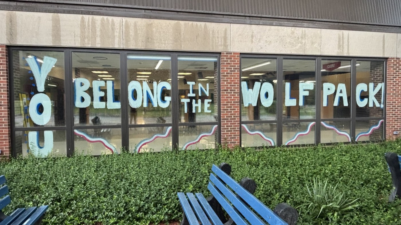 A building has large glass windows displaying a message. Benches are in front of the building.