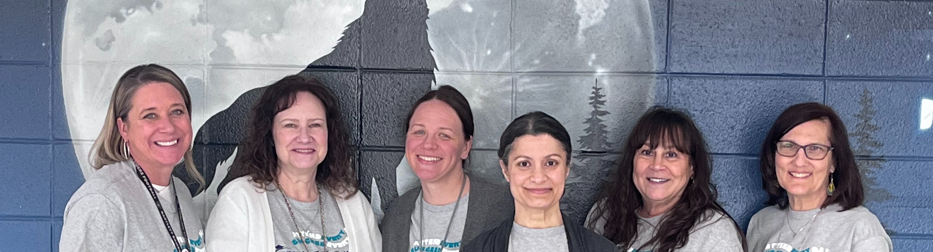 A group of six women poses for a photo in front of a wall mural featuring a large moon.