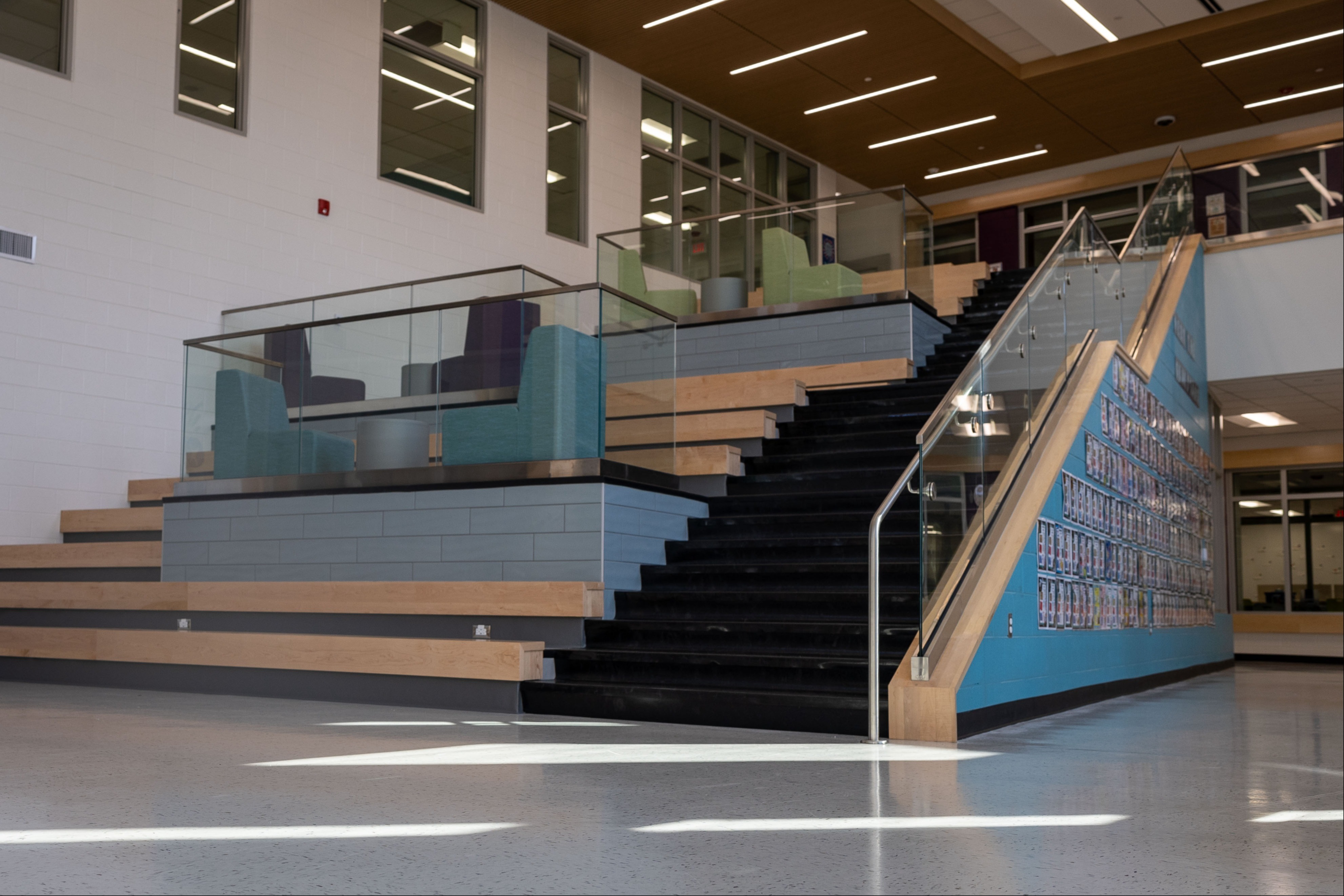 An empty, well-lit indoor area with a staircase featuring black steps, glass railings, and a blue tiled platform.