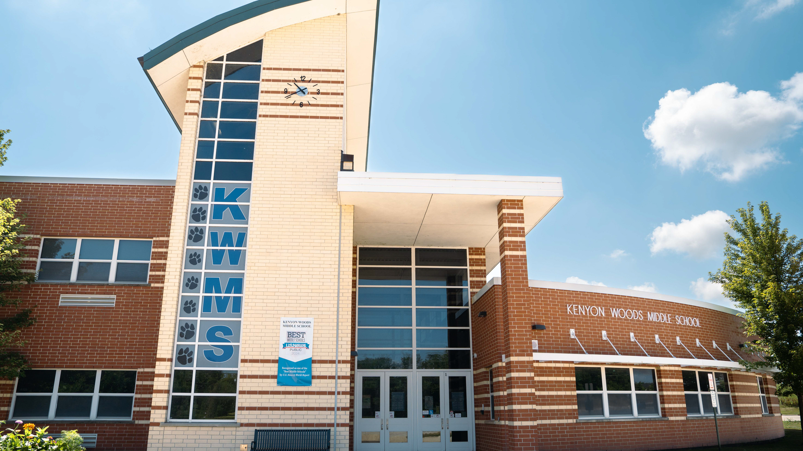 A school building with a blue sign reading "KEMME". Large windows, a blue sky with clouds.