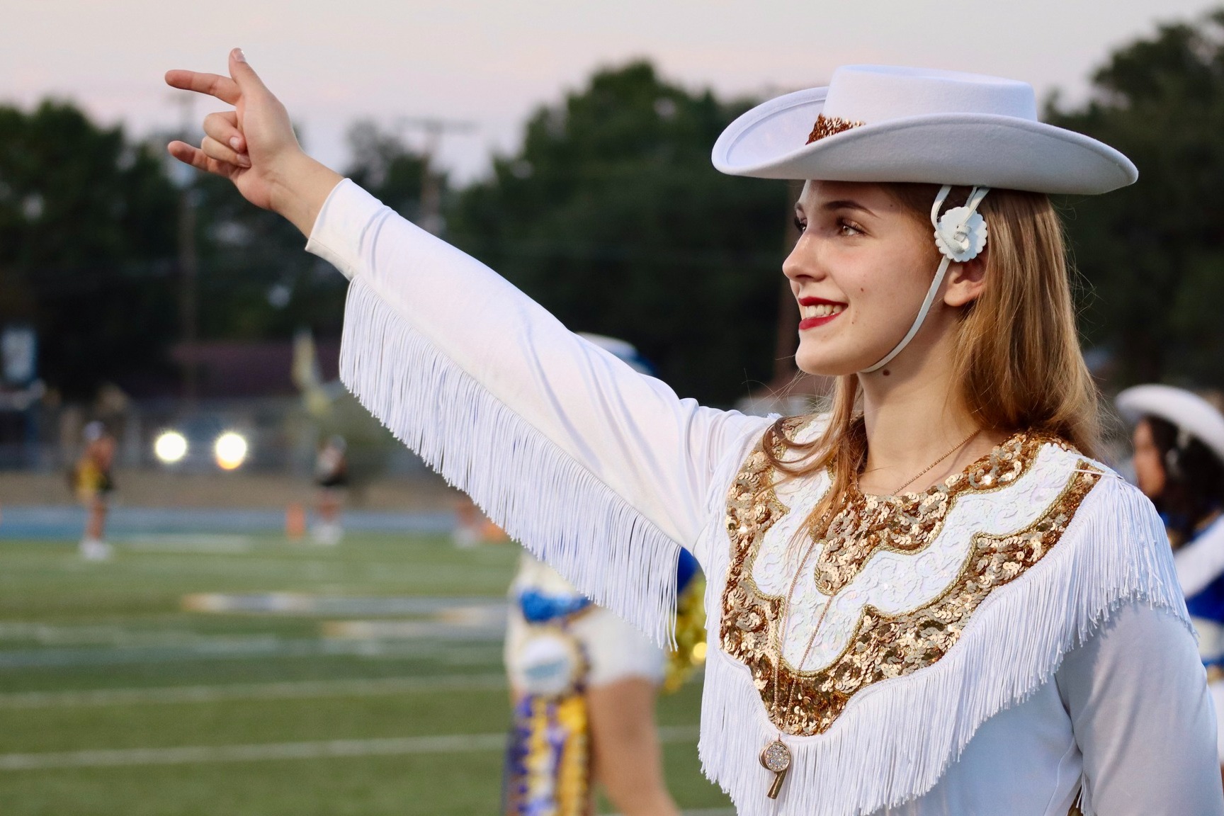 Female Golden Girls Dancer in white uniform holding up arm while singing school song.